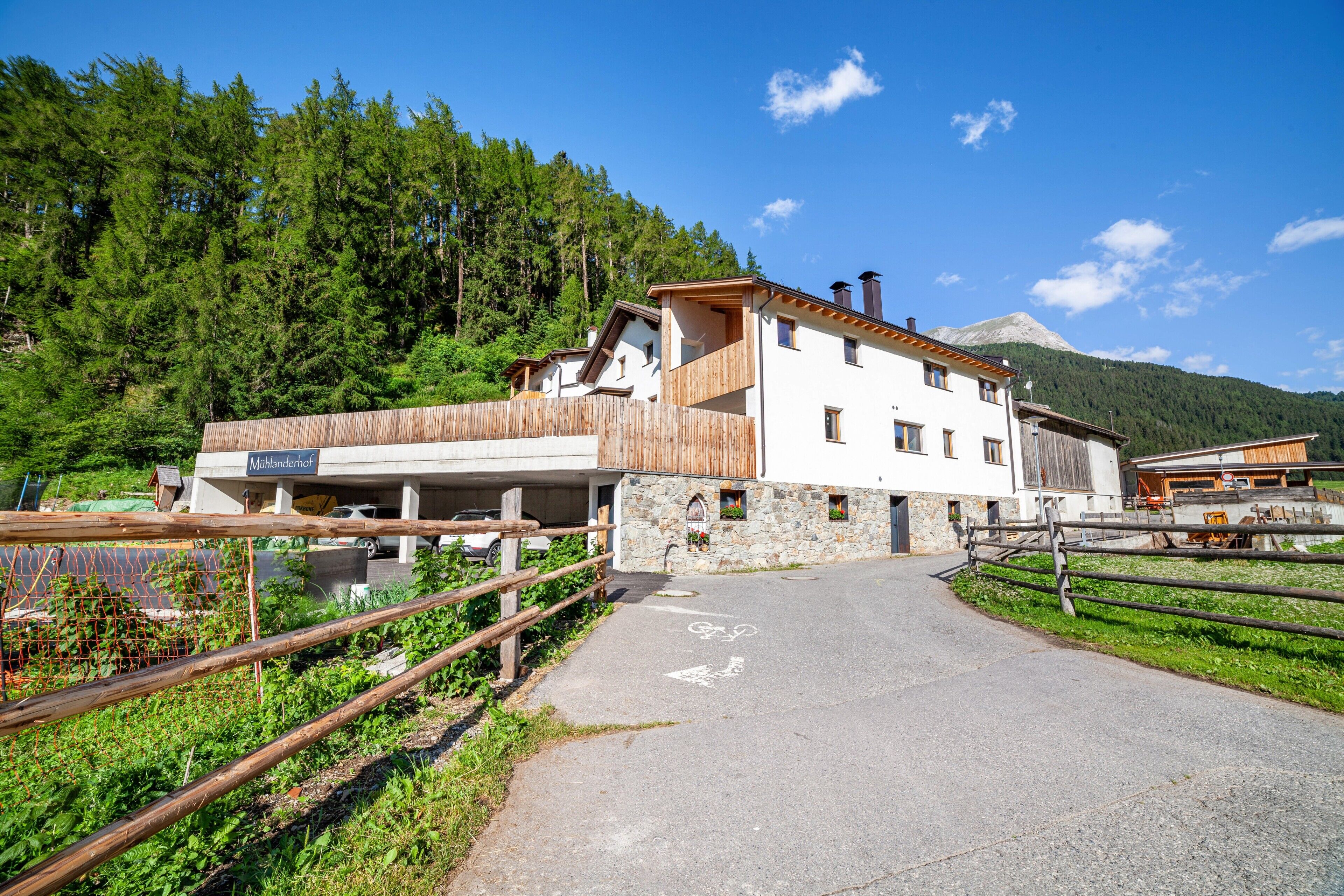 A two-story building with a balcony, a stone wall, and a mountain in the background.