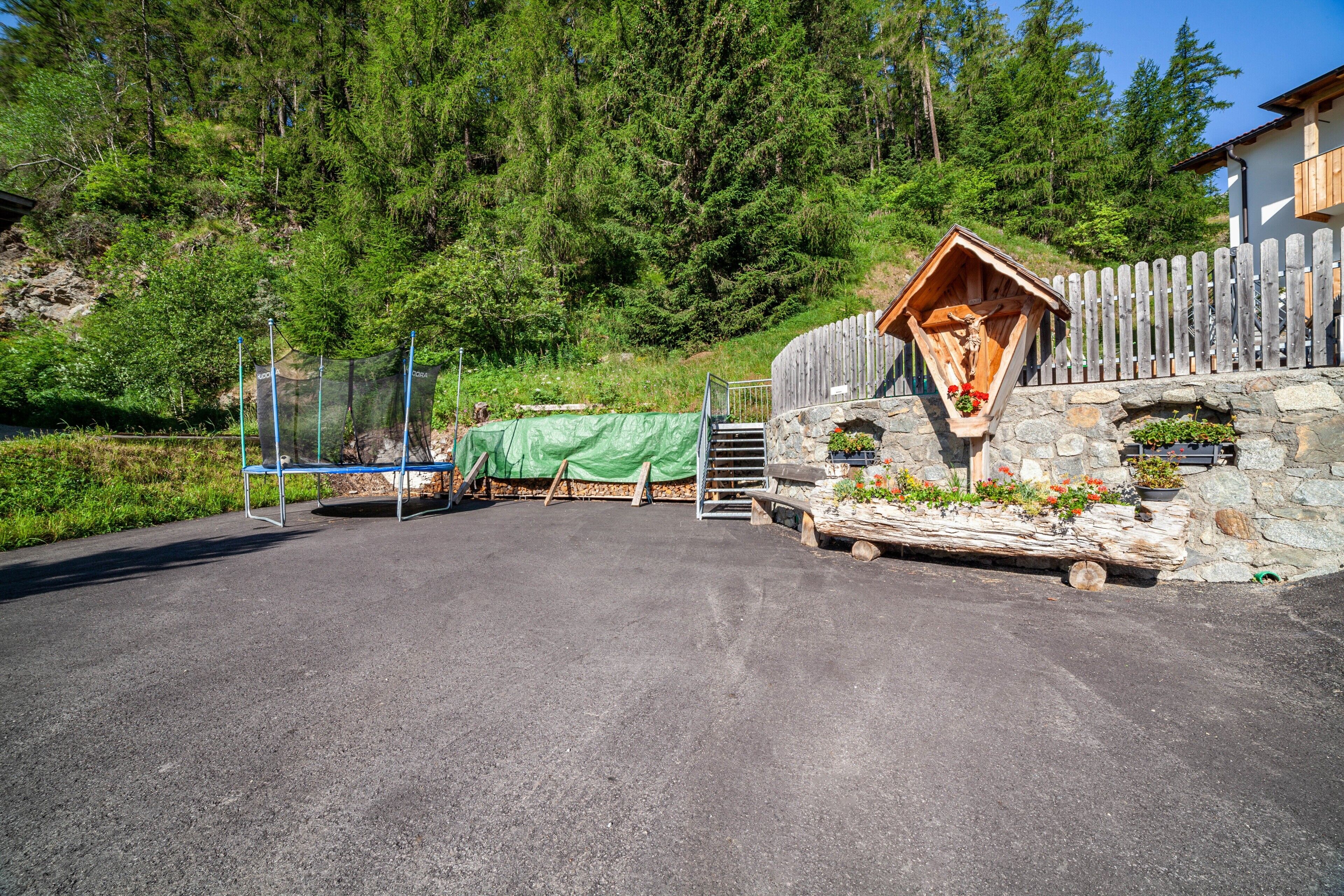 Un bâtiment rustique en bois, doté de fondations en pierre, entouré d’une clôture en bois et d’une végétation luxuriante.