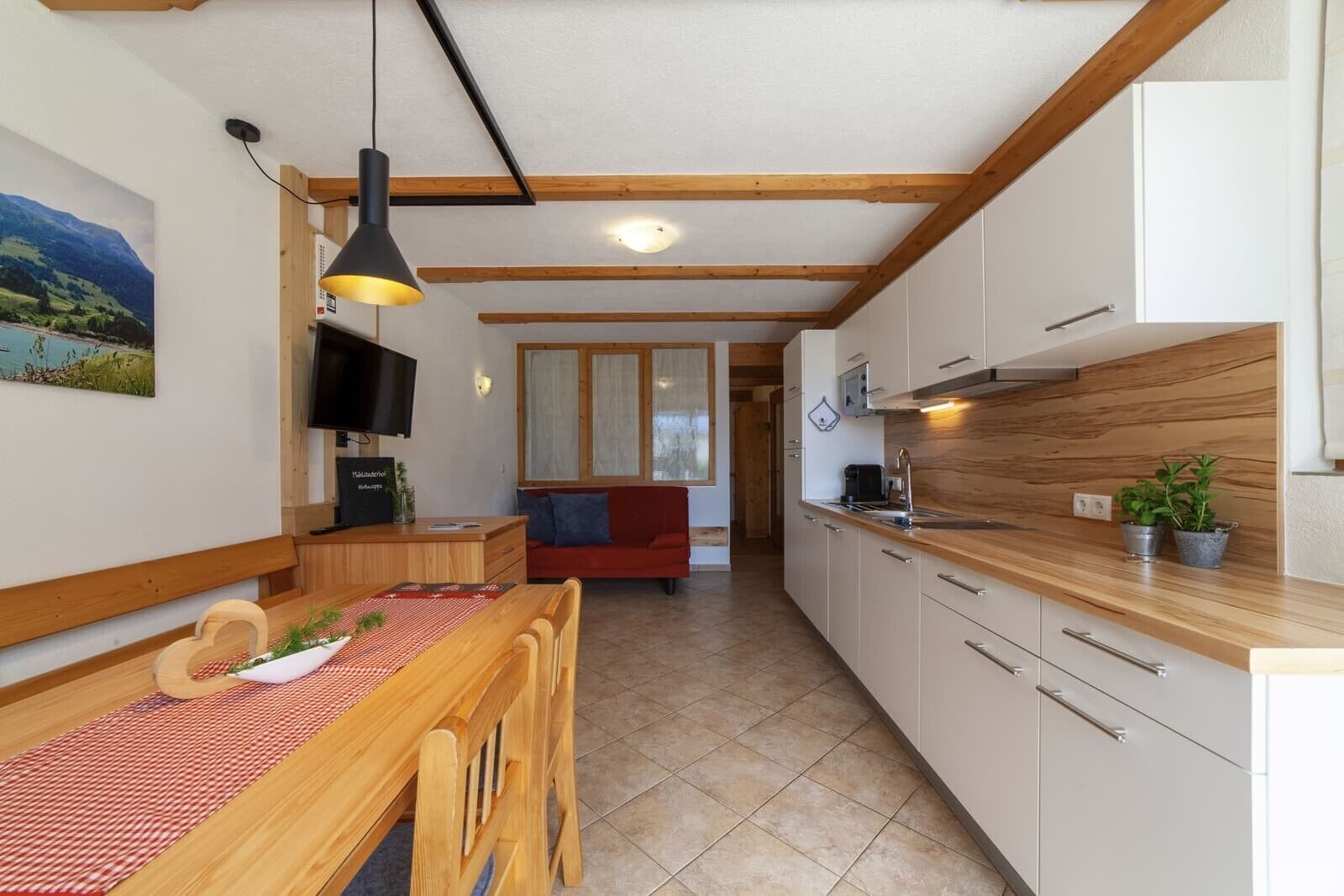 Een moderne keuken met houten kastjes, een eettafel met stoelen, een televisie en een rode bank op de achtergrond.