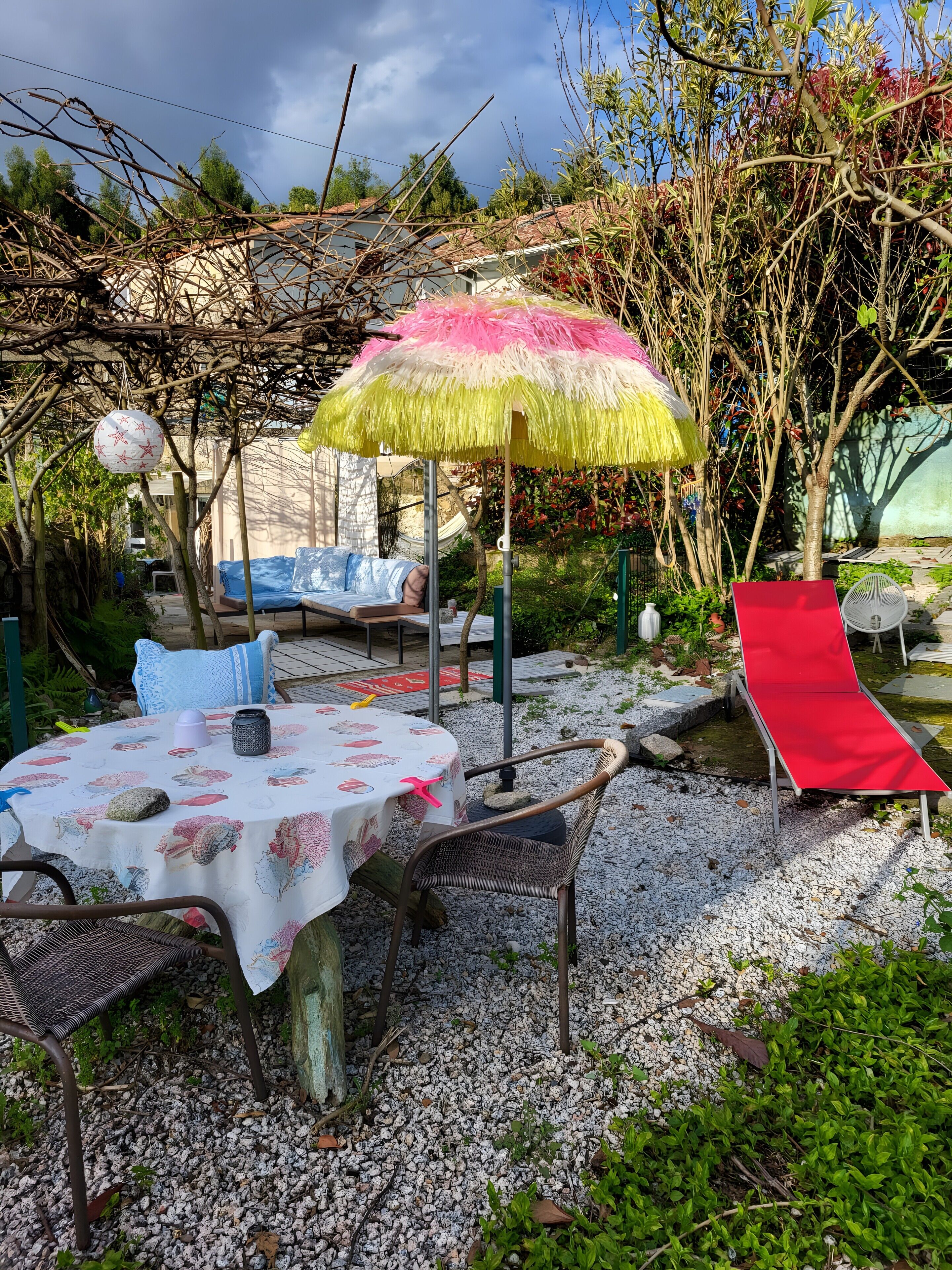 Un patio jardín con una mesa, sillas, una butaca roja y un paraguas decorativo.