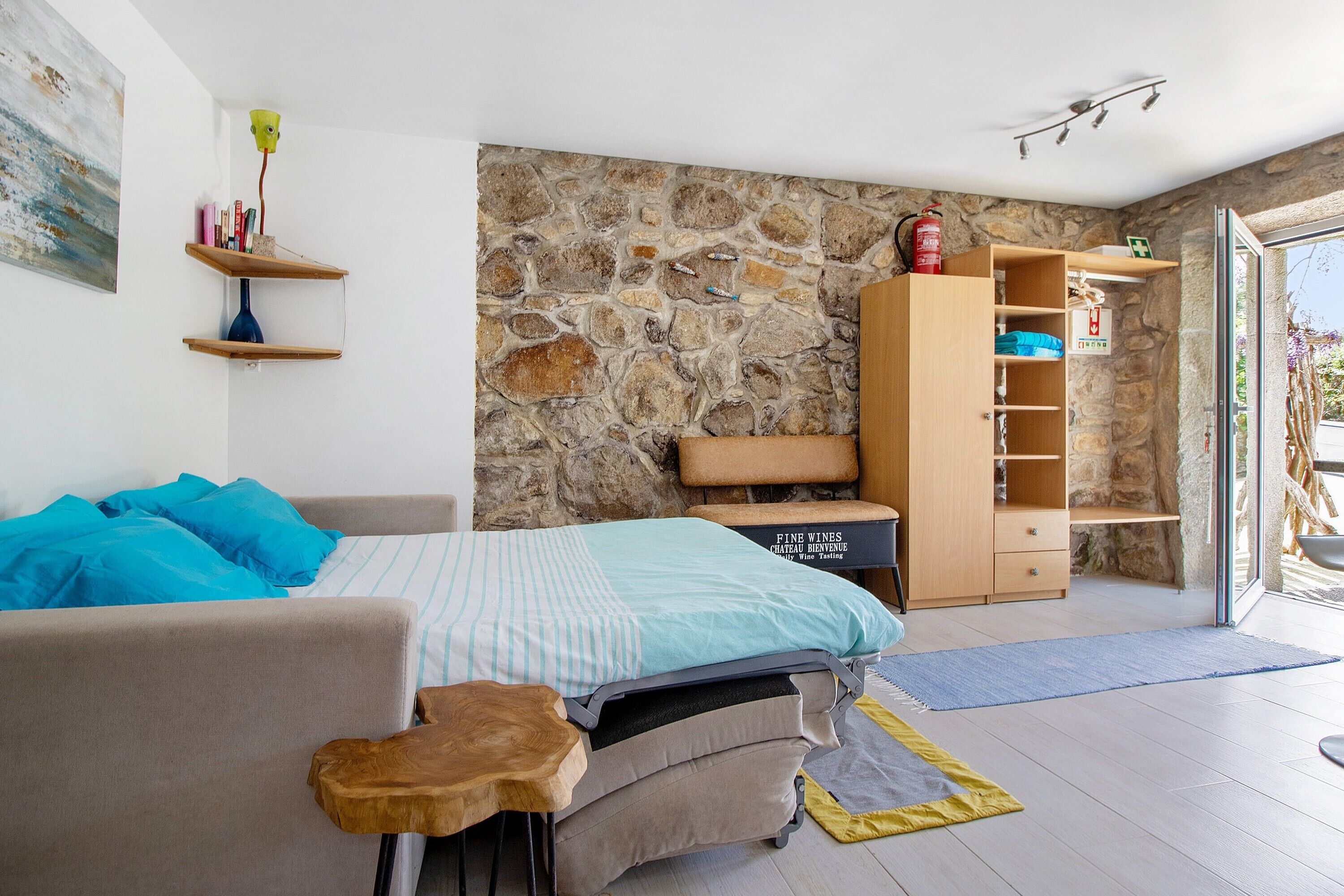 Une chambre à coucher avec un lit, une armoire en bois, un mur en pierre et une porte donnant sur un balcon.