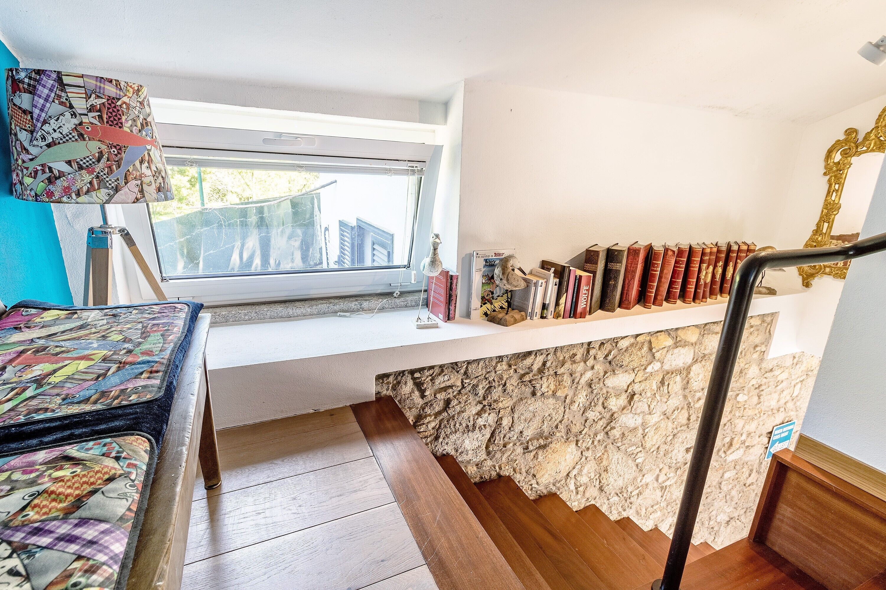 A room with a window, a bookshelf, a patterned table, and a staircase.