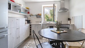 A kitchen with white cabinets, a round table, and a window. - Holiday Home 'Casa Azul' with Mountain View, Shared Pool and Wi-Fi (Moledo)