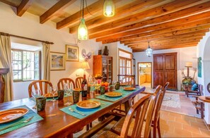 A dining area with wooden tables and chairs, a kitchen in the background, and a rustic ceiling. - Country House 'Cerdà' with Mountain View, Wi-Fi and Air Conditioning (Pollensa)