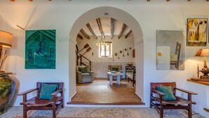Ampla sala de estar com teto alto, vigas de madeira e um arco central que dá acesso a uma área de jantar.