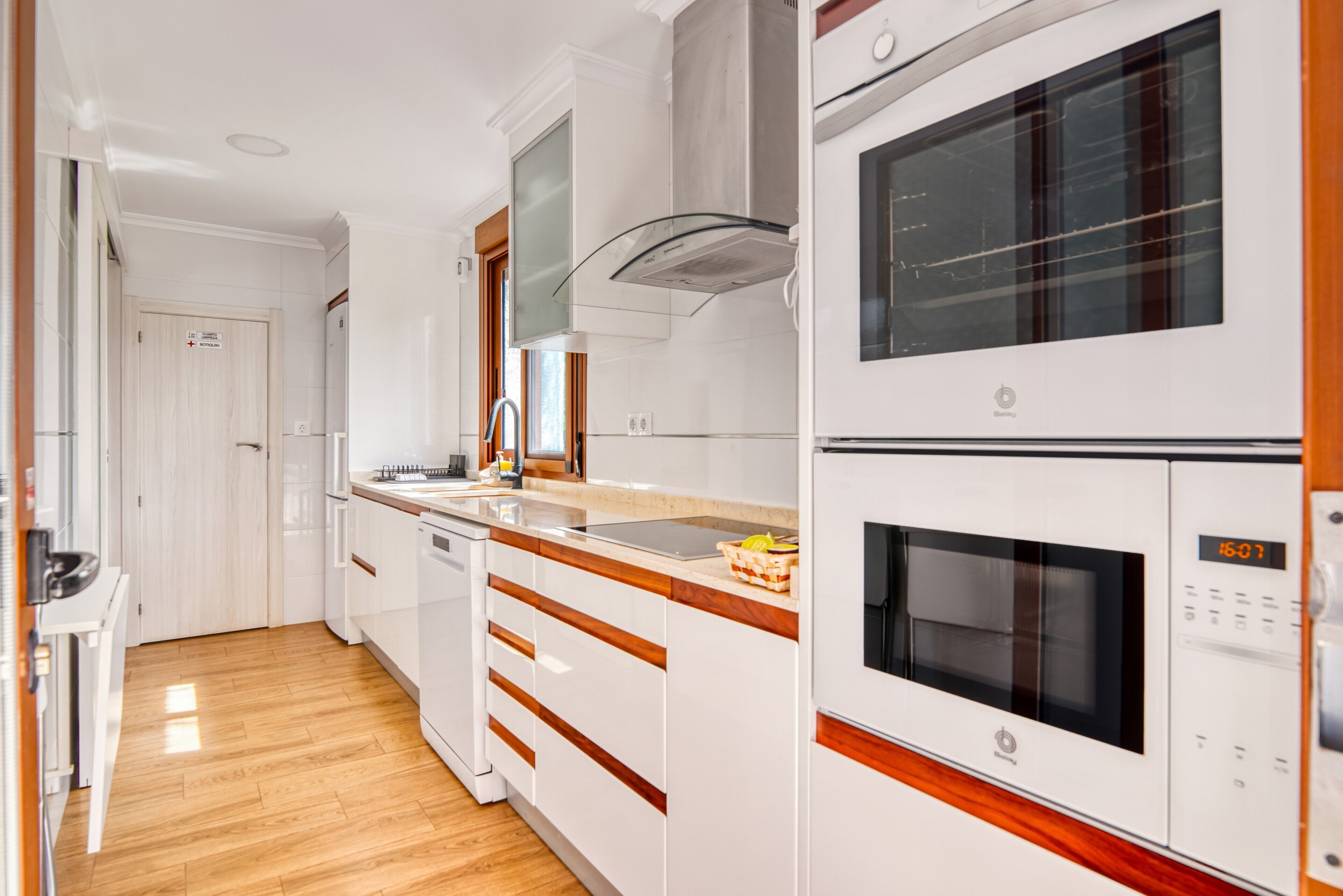 Une cuisine avec des armoires blanches, une hotte de cuisinière en acier inoxydable, un four à micro-ondes et un four double.