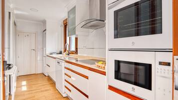 Une cuisine avec des armoires blanches, une hotte de cuisinière en acier inoxydable, un four à micro-ondes et un four double.