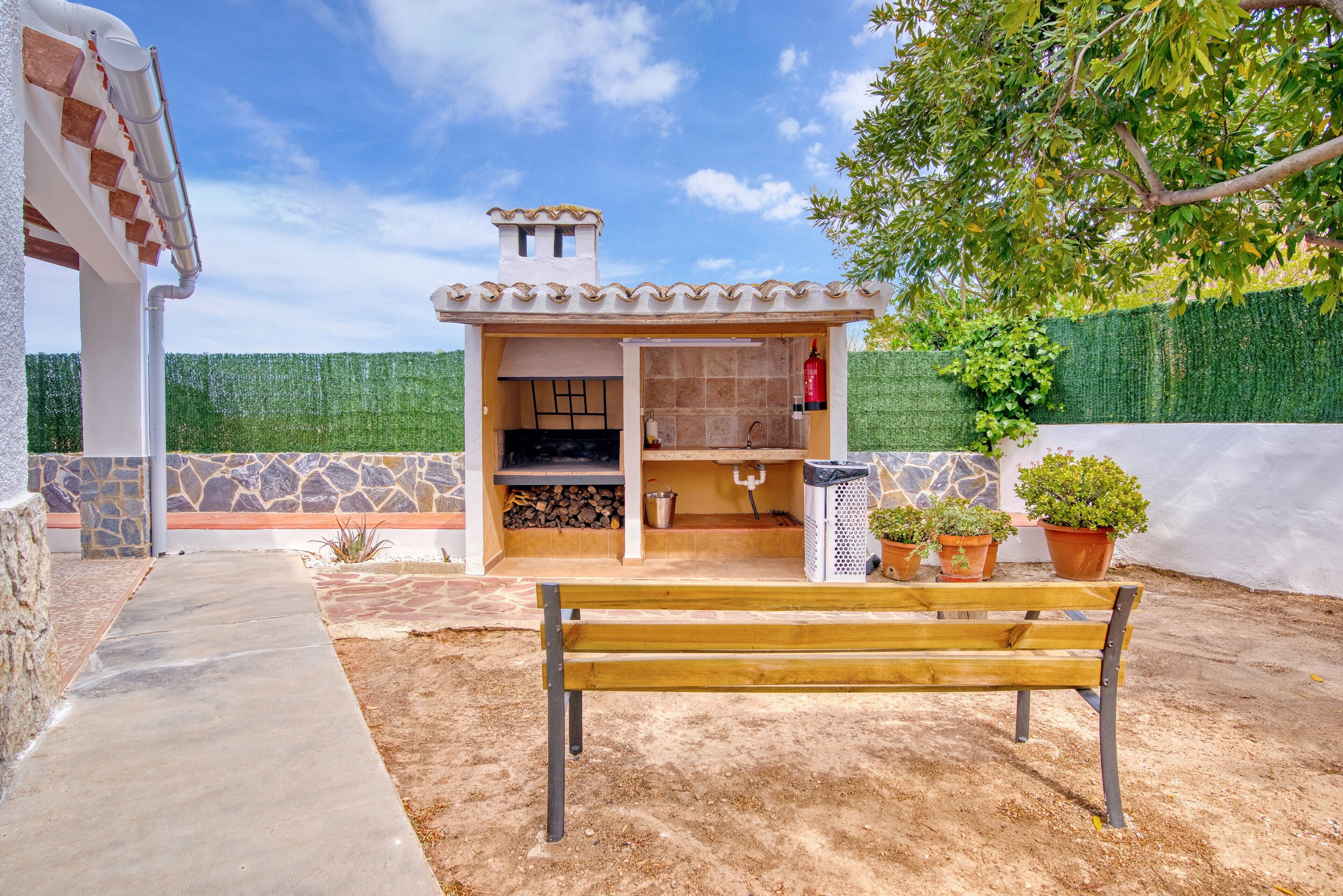 A patio with a wooden bench, a barbecue area, and potted plants.
