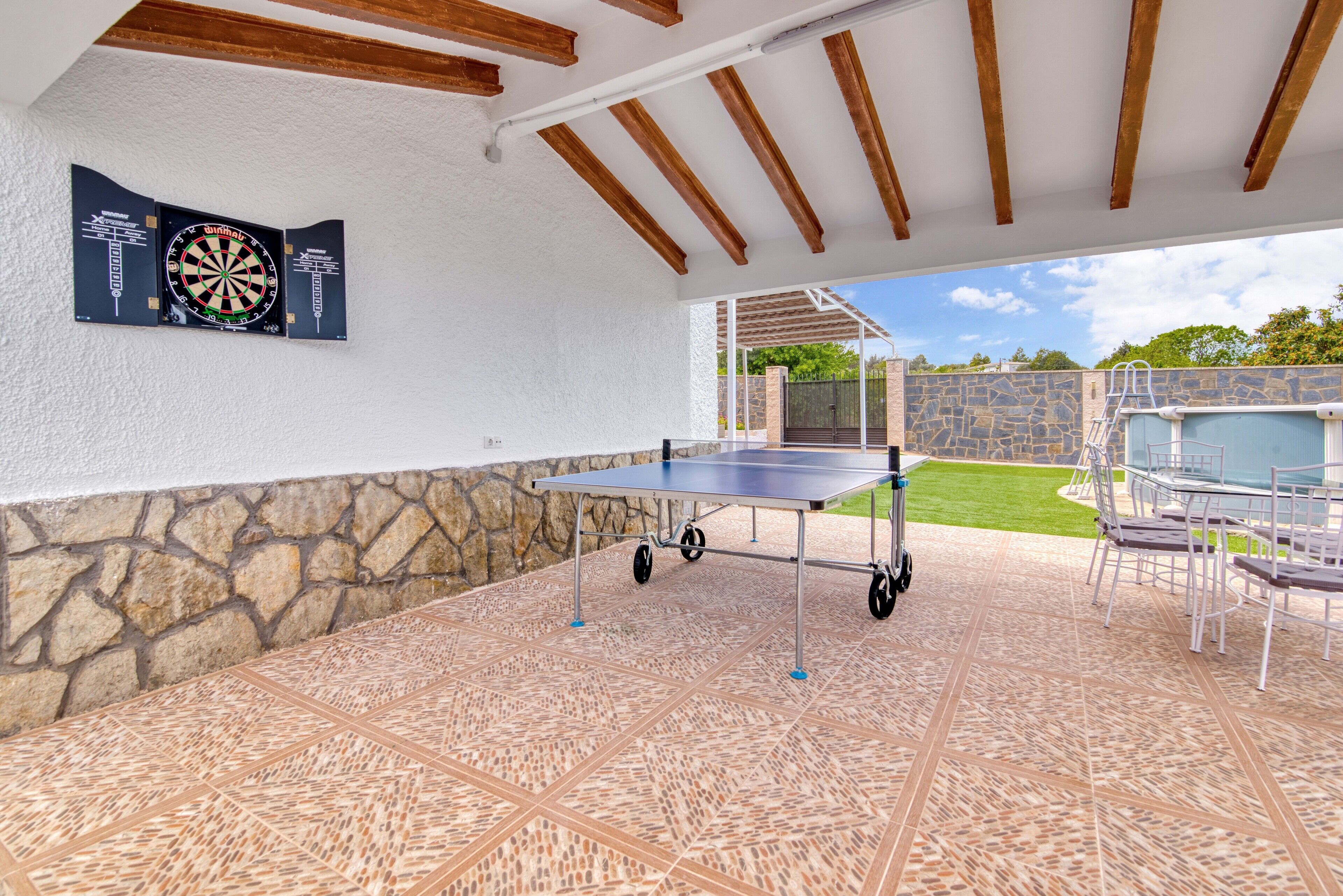 Un patio couvert comprenant une table de ping-pong, un mur en pierre et des sièges d’extérieur.