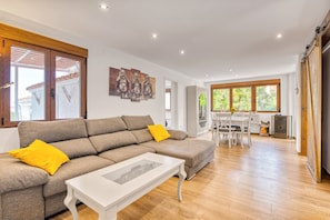 En moderne stue med en hjørnesofa, et hvidt sofabord og et spiseområde med et bord og stole.