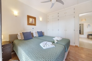 A bedroom with a bed, bedside tables, a wardrobe, a ceiling fan, and a framed picture on the wall.