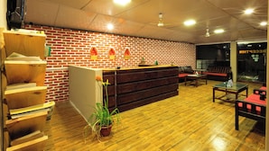 A reception area with a brick wall, wooden reception desk, seating area, and a potted plant. - Safari Club (Sauraha)