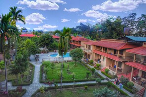 A courtyard with a swimming pool, surrounded by lush greenery and palm trees. - Safari Club (Sauraha)