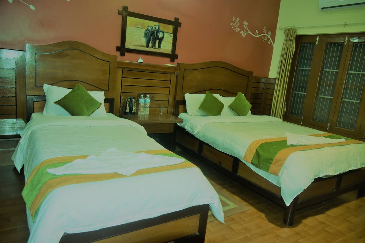 A hotel room with two single beds, wooden headboards, a nightstand with a lamp, a framed picture on the wall, and a window with curtains.