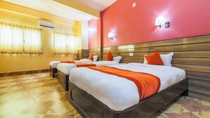 A hotel room with three beds, a wooden headboard, and a red accent wall. - Safari Club (Sauraha)