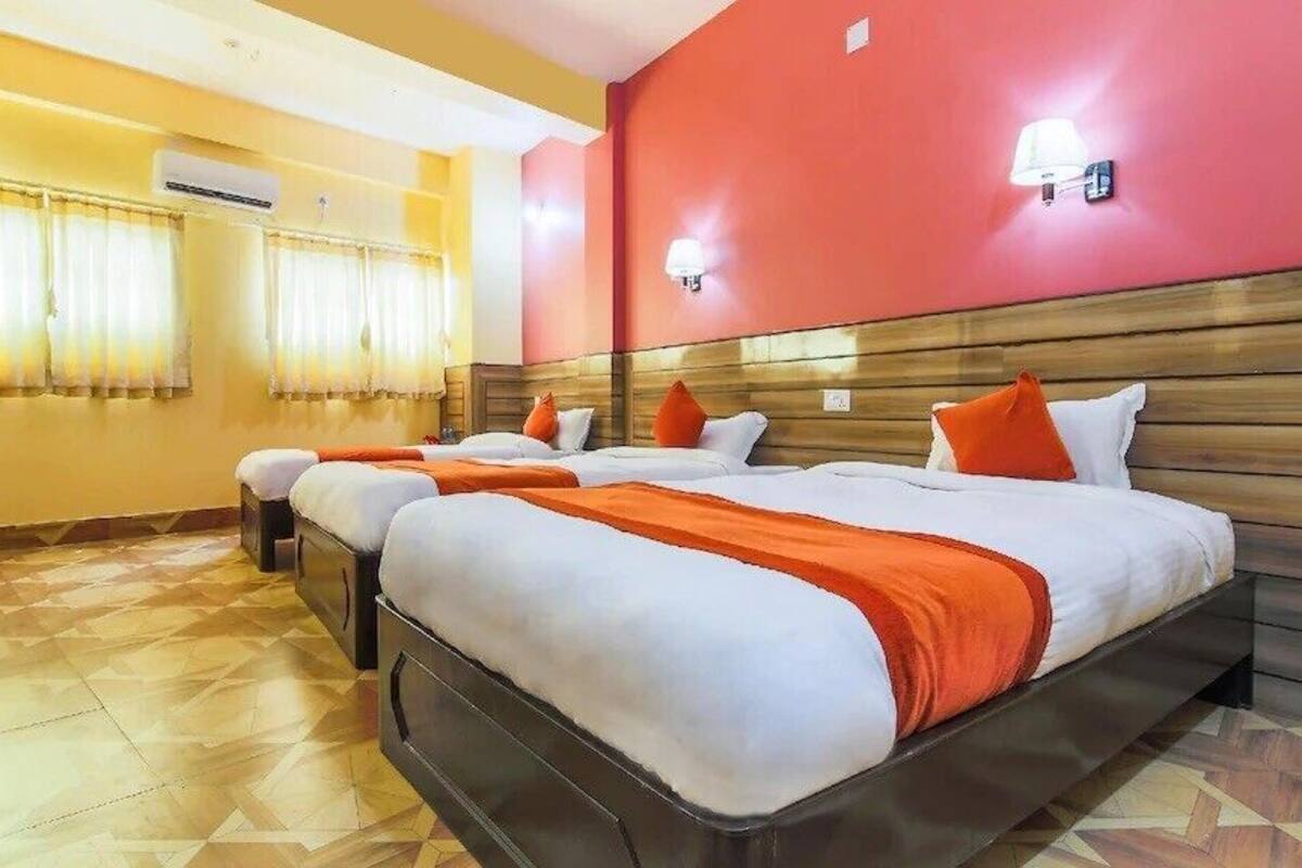 A hotel room with three beds, a wooden headboard, and a red accent wall.