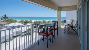 Een balkon met uitzicht op het strand, een tafel met stoelen en een hekwerk.