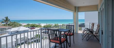 A balcony with a view of the beach, a table with chairs, and a railing.