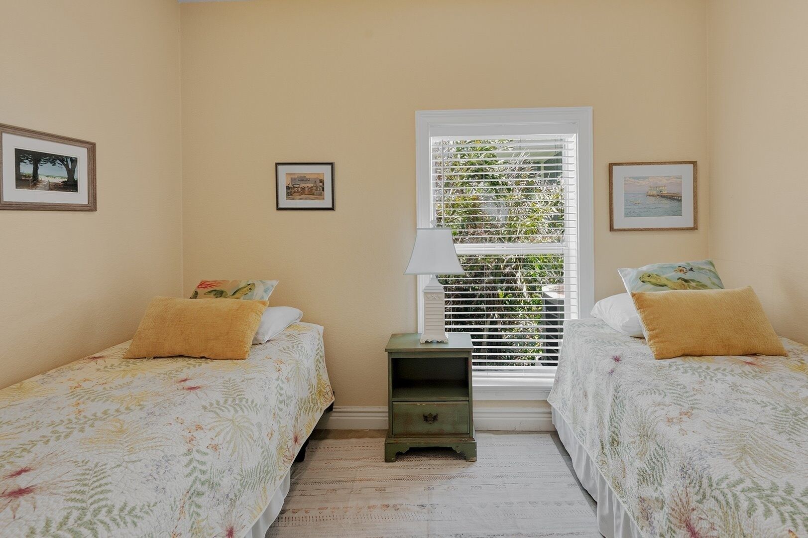 Une chambre avec deux lits simples, une table de chevet et une fenêtre avec des stores.