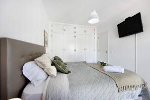 Une chambre à coucher comprenant un lit, une armoire, un téléviseur et un luminaire suspendu.