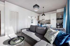 Un salon moderne avec un canapé gris, une petite table basse et un coin repas à l’arrière-plan.