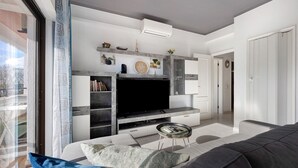 A modern living room with a flat-screen TV, a sofa, a coffee table, and a bookshelf. - Apartment "Refúgio Praia da Rocha" with Sea View, Balcony & Wi-Fi (Portimão)