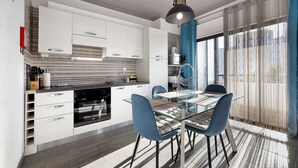 A modern kitchen with white cabinets, a glass dining table, and blue chairs. - Apartment "Refúgio Praia da Rocha" with Sea View, Balcony & Wi-Fi (Portimão)