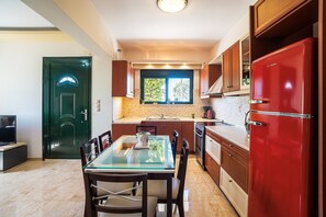 A compact kitchen with a dining area, a red refrigerator, wooden cabinets, and a window. - Holiday Home 'Casa D' Irene' with Sea View, Wi-Fi and Air Conditioning (Rhodes)