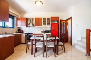 A kitchen with wooden cabinets, a red refrigerator, a dining table with chairs, and a microwave.