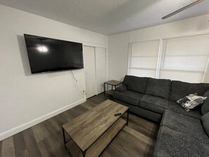 A living room with a flat-screen TV mounted on the wall, a dark-colored sofa, a wooden coffee table, and a small side table.