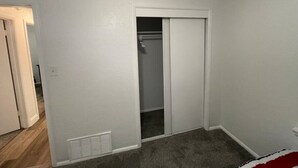 Una habitación con una puerta blanca que da a un armario, un respiradero en el suelo y piso alfombrado.