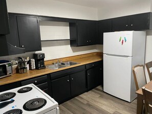 Eine Küche mit schwarzen Schränken, einem weißen Kühlschrank, einer Mikrowelle, einer Kaffeemaschine und einer Holzarbeitsplatte.