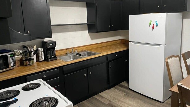 Una cocina compacta con armarios negros, un refrigerador blanco, microondas, cafetera y encimera de madera.