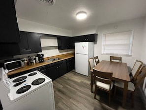 A compact kitchen with a stove, microwave, refrigerator, and wooden dining table with chairs. - Spacious 3-Bedroom Home Convenient to Fort Sill (Lawton)