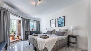 A modern bedroom with a large bed, a bedside table, a bench, and a view of the outdoors. - Holiday Home 'Beachfront Luxury Villa La Cala' with Private Pool, Wi-Fi and Air Conditioning (Las Lagunas de Mijas)