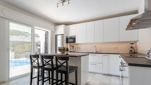 A modern kitchen with a large island, white cabinetry, and a view of a swimming pool. - Holiday Home 'Beachfront Luxury Villa La Cala' with Private Pool, Wi-Fi and Air Conditioning (Las Lagunas de Mijas)