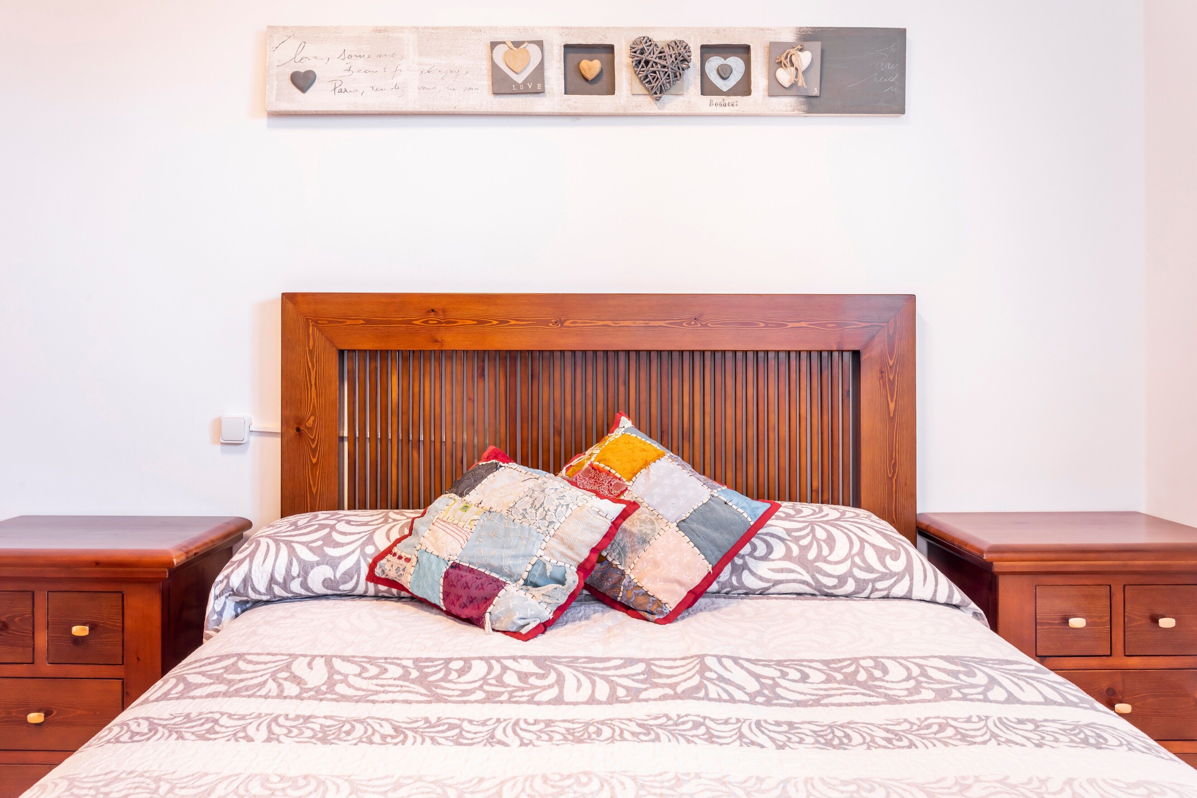 A bed with a wooden headboard, two nightstands, and a wall decoration above the bed.