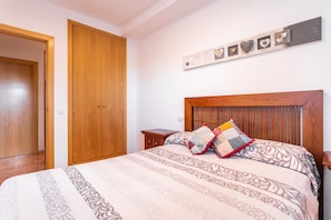 A bedroom with a wooden headboard, a bed with patterned bedding, a nightstand, and a wall-mounted decoration. - Apartment "Balcón Del Mar" with Shared Pool & Private Terrace (Canet d'en Berenguer)