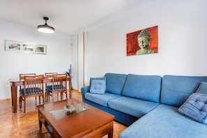 A living room with a blue sofa, wooden dining table, chairs, and a ceiling light fixture. - Apartment "Balcón Del Mar" with Shared Pool & Private Terrace (Canet d'en Berenguer)