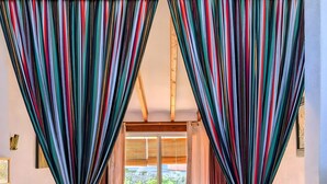 Ein Schlafzimmer mit Bett, Vorhängen, einem Fenster und Blick ins Grüne.