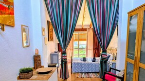 Ein Zimmer mit einem Bett, einem Sessel, einem kleinen Tisch und einem Fenster mit Vorhängen.
