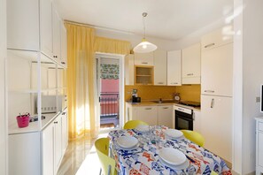 Une cuisine de taille réduite avec des meubles blancs, une table à manger pour quatre personnes et un rideau jaune.
