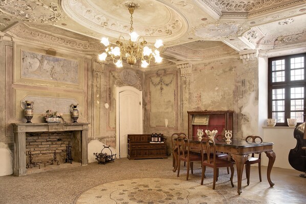 A room with a fireplace, a chandelier, a wooden table with chairs, and a piano.
