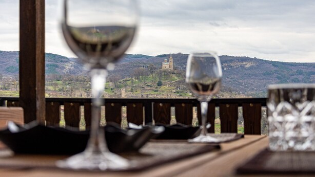 Une table avec deux verres à vin et un verre d’eau, le tout placé devant un paysage montagneux avec un château en arrière-plan.