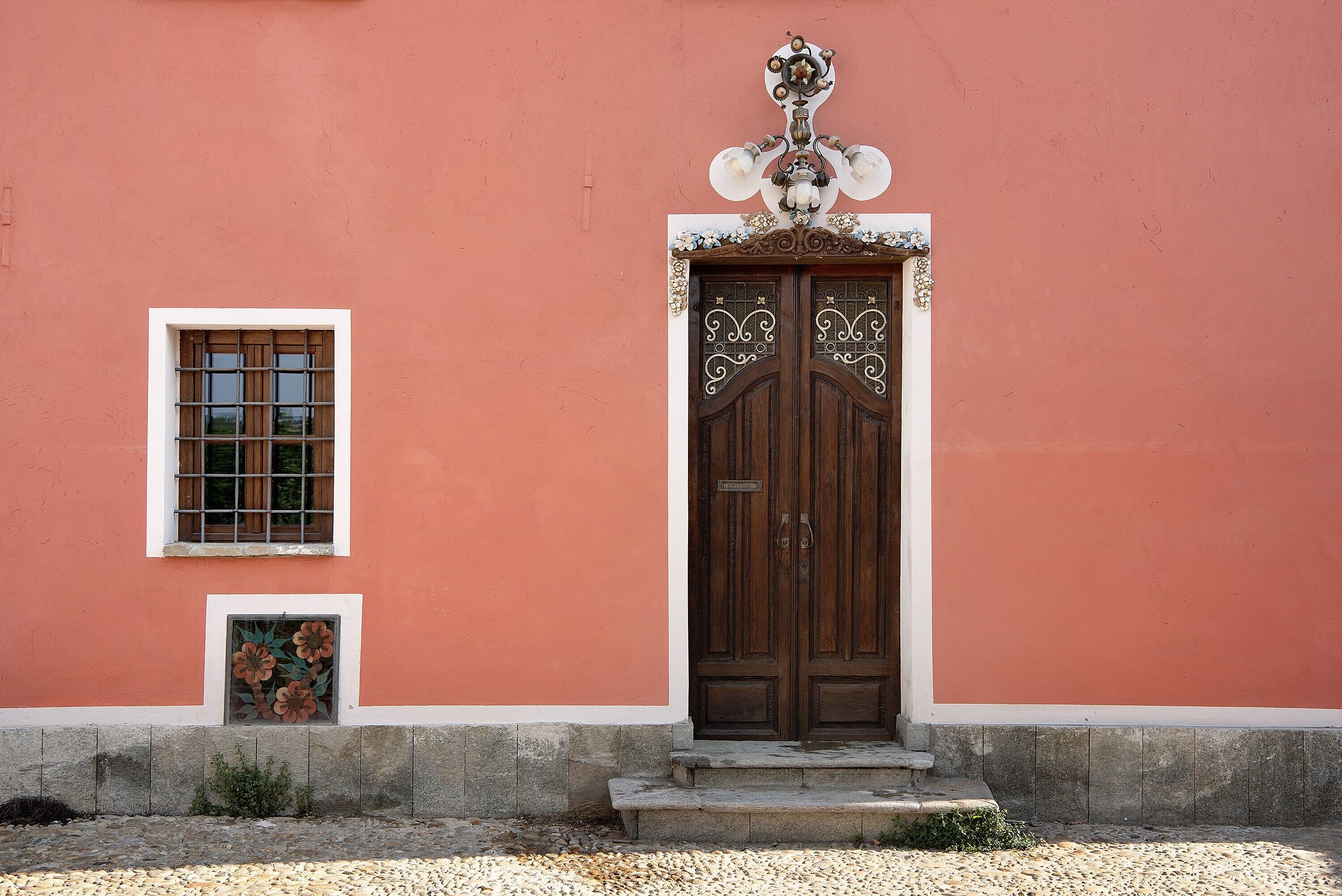 Un edificio con un'ampia porta in legno a due battenti, una piccola finestra a griglia e un cartello decorativo sopra la porta.