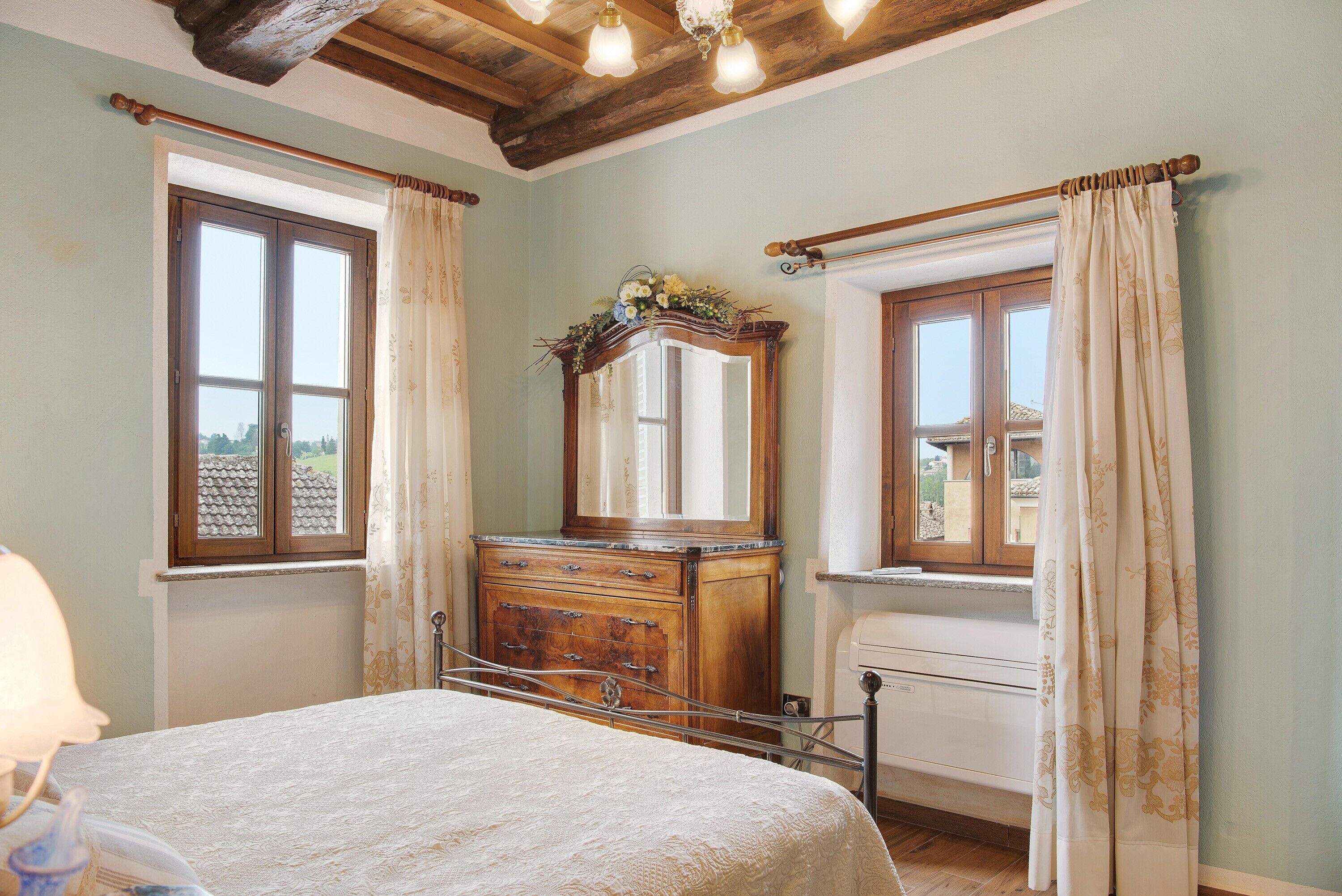 Une chambre à coucher avec un lit, une commode, un miroir et deux fenêtres avec des rideaux.