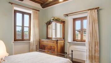 Une chambre à coucher avec un lit, une commode, un miroir et deux fenêtres avec des rideaux.