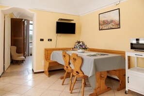 A dining area with a table, chairs, a television, and a painting on the wall. - Apartment 'La Rocca di Efisio - Grignolino' with Balcony, Wi-Fi and Air Conditioning (Costigliole d'Asti)