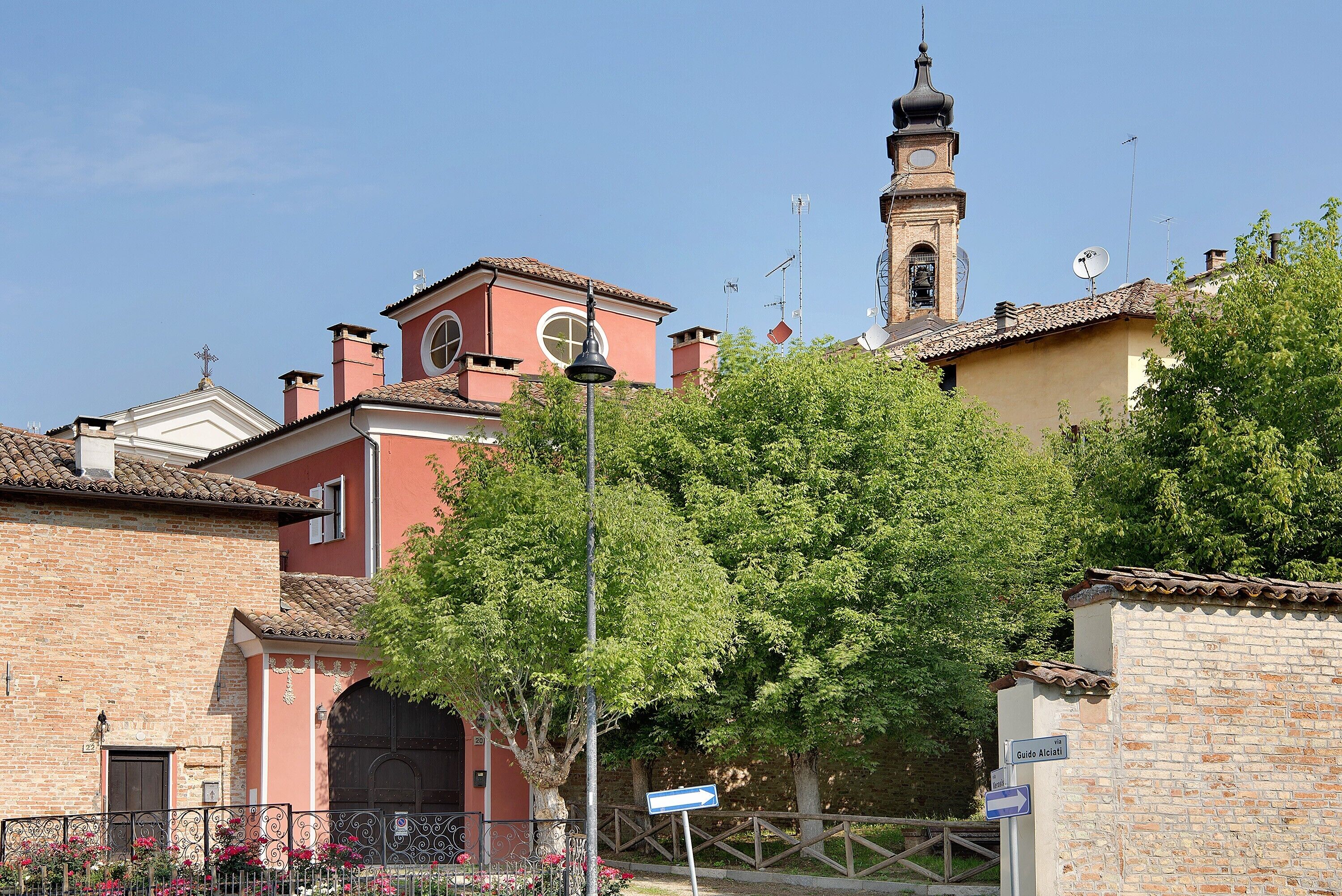 A traditional building with a bell tower, a sign indicating a direction, and a tree in the foreground.