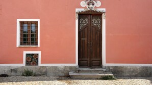 A building with a large wooden double door, a small window with a grid pattern, and a decorative sign above the door. - Apartment 'La Rocca di Efisio - Grignolino' with Balcony, Wi-Fi and Air Conditioning (Costigliole d'Asti)